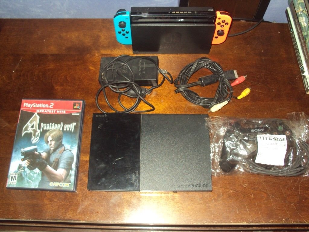 Consolas, cables y un juego de PlayStation 2 sobre la mesa.